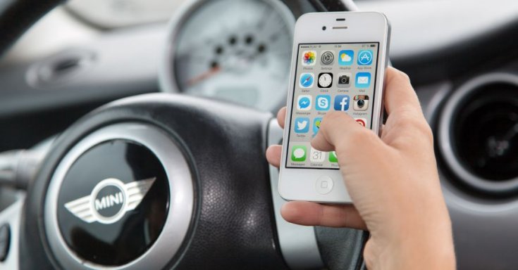 iPhone-t tartó kéz egy Mini volánja mögött